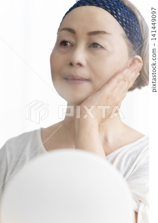 A senior woman uses a facial steamer to perform a self-care facial. A senior woman uses a facial steamer to perform a self-care facial. 141449097