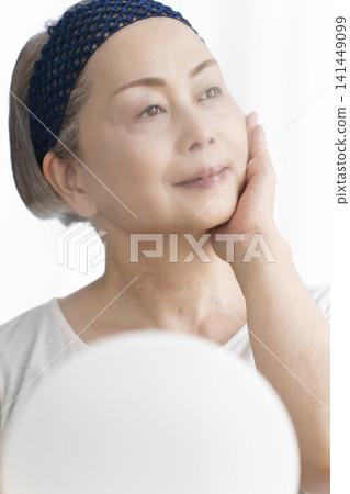 A senior woman uses a facial steamer to perform a self-care facial. A senior woman uses a facial steamer to perform a self-care facial. 141449099