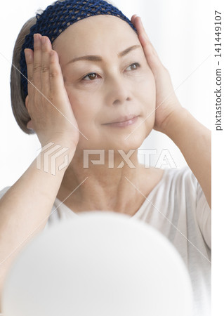 A senior woman uses a facial steamer to perform a self-care facial. A senior woman uses a facial steamer to perform a self-care facial. 141449107