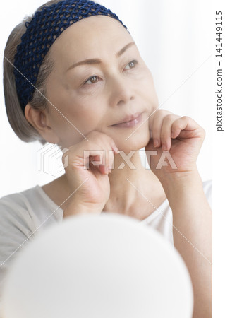 A senior woman uses a facial steamer to perform a self-care facial. A senior woman uses a facial steamer to perform a self-care facial. 141449115