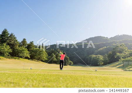 A golfer's dynamic swing as they hit a driver shot under a blue sky. 141449167