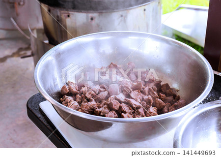 Small pieces of beef are being cooked in metal bowl over hot stove in an outdoor setting. Small pieces of beef are being cooked in metal bowl over hot stove in an outdoor setting. 141449693