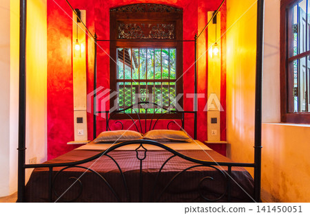 Elegant tropical bedroom with four-poster bed and vibrant red accent wall Elegant tropical bedroom with four-poster bed and vibrant red accent wall 141450051