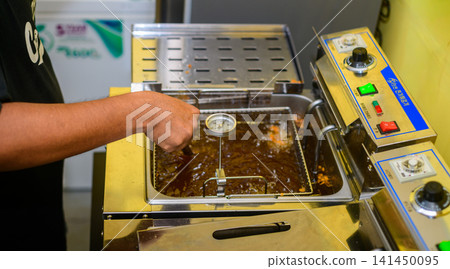 Chef checking deep fryer temperature while preparing fried food in a commercial kitchen Chef checking deep fryer temperature while preparing fried food in a commercial kitchen 141450095