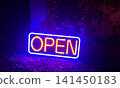 Open neon sign glowing in blue and yellow light for a retail storefront or business entrance 141450183