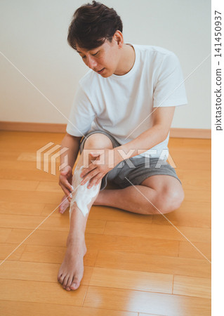 畫面中,一位四十多歲的男子坐在地板上,準備刮腿毛。 畫面中,一位四十多歲的男子坐在地板上,準備刮腿毛。 141450937