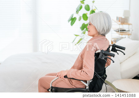A senior woman with gray hair in a wheelchair in her living room at home and in a hospital room. A senior woman with gray hair in a wheelchair in her living room at home and in a hospital room. 141451088