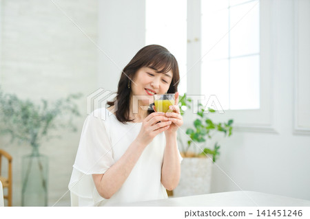 一位六十多歲的婦女在客廳喝蔬菜汁。 一位六十多歲的婦女在客廳喝蔬菜汁。 141451246
