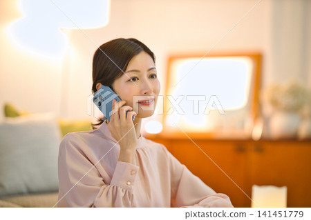 A woman in her 40s relaxing in her room at night and looking at her smartphone. A woman in her 40s relaxing in her room at night and looking at her smartphone. 141451779