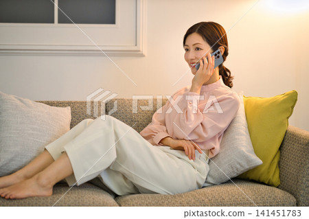 A woman in her 40s relaxing in her room at night and looking at her smartphone. A woman in her 40s relaxing in her room at night and looking at her smartphone. 141451783