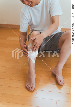 A Japanese man in his 40s sits on the floor and applies shaving foam to his shin. A Japanese man in his 40s sits on the floor and applies shaving foam to his shin. 141451884