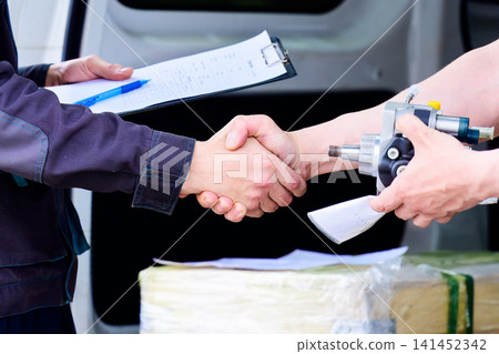 Mechanic and customer shaking hands over high pressure fuel pump transaction delivery with test report and car parts clipboard Mechanic and customer shaking hands over high pressure fuel pump transaction delivery with test report and car parts clipboard 141452342