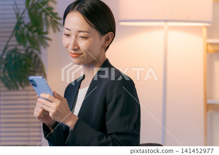 一位身穿西裝的女士在夜裡看著她的智慧型手機。 一位身穿西裝的女士在夜裡看著她的智慧型手機。 141452977