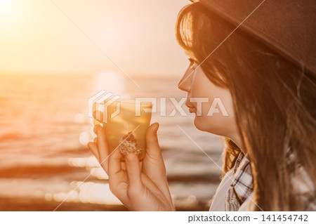Sunset woman drink holding a warm beverage on the beach during golden hour 141454742