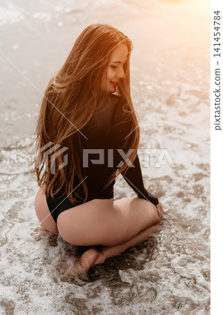 Woman beach ocean kneeling in foamy surf on a sandy shore at sunset during a relaxing summer vacation Woman beach ocean kneeling in foamy surf on a sandy shore at sunset during a relaxing summer vacation 141454784