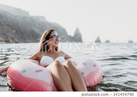 Woman, relaxing, floating in donut ring in ocean with cliffs, enjoying summer holiday with copy space. 141454790