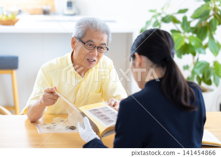 現場鑑定服務:一位老人在家中請人鑑定他的郵票和古幣。 現場鑑定服務:一位老人在家中請人鑑定他的郵票和古幣。 141454866