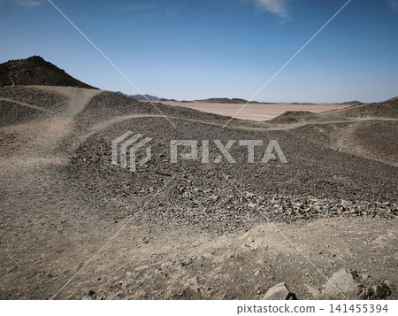 Vast Egyptian desert panorama with rolling sand dunes, rugged rocky terrain, and a clear blue sky, showcasing the dramatic beauty and serene emptiness of the arid landscape under bright sunlight. Vast Egyptian desert panorama with rolling sand dunes, rugged rocky terrain, and a clear blue sky, showcasing the dramatic beauty and serene emptiness of the arid landscape under bright sunlight. 141455394