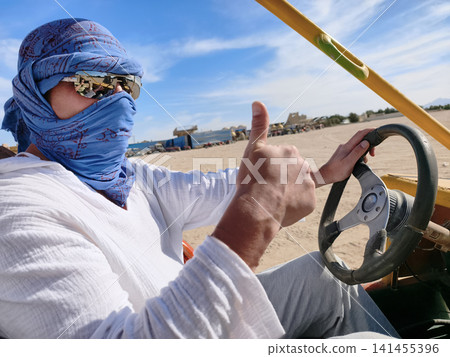 Desert thrill ride Arab man in traditional attire drives a dune buggy across the sun drenched sands, capturing the excitement of off road adventure under a clear blue sky. 141455396