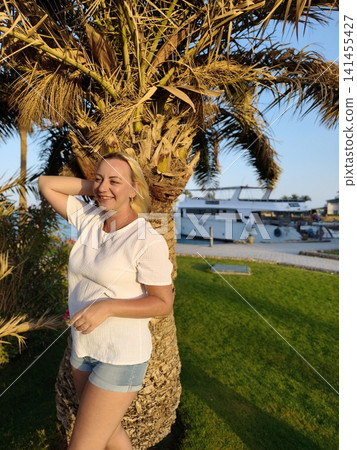 Serene coastal moment a relaxed woman crisp white t shirt smiles gently against backdrop swaying palm trees and tranquil sea, embodying the calm beauty perfect seaside getaway under soft golden sky Serene coastal moment a relaxed woman crisp white t shirt smiles gently against backdrop swaying palm trees and tranquil sea, embodying the calm beauty perfect seaside getaway under soft golden sky 141455427