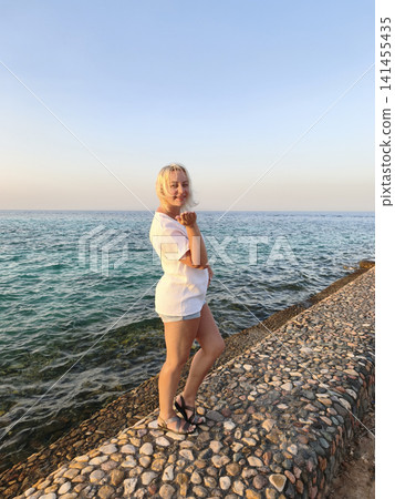 Joyful freedom by the sea carefree woman in crisp white top celebrates the moment with arms raised on a rocky shore, surrounded the calming rhythm of waves and the vast horizon under a clear blue sky Joyful freedom by the sea carefree woman in crisp white top celebrates the moment with arms raised on a rocky shore, surrounded the calming rhythm of waves and the vast horizon under a clear blue sky 141455435