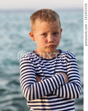 Young boy in a classic striped shirt stands confidently sea, his varied expressions capturing curiosity, contemplation, and carefree joy timeless portrait that tells story of childhood by shore. Young boy in a classic striped shirt stands confidently sea, his varied expressions capturing curiosity, contemplation, and carefree joy timeless portrait that tells story of childhood by shore. 141455439