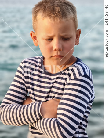 Young boy in a classic striped shirt stands confidently sea, his varied expressions capturing curiosity, contemplation, and carefree joy timeless portrait that tells story of childhood by shore. Young boy in a classic striped shirt stands confidently sea, his varied expressions capturing curiosity, contemplation, and carefree joy timeless portrait that tells story of childhood by shore. 141455440
