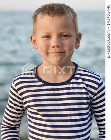 Young boy in a classic striped shirt stands confidently sea, his varied expressions capturing curiosity, contemplation, and carefree joy timeless portrait that tells story of childhood by shore. Young boy in a classic striped shirt stands confidently sea, his varied expressions capturing curiosity, contemplation, and carefree joy timeless portrait that tells story of childhood by shore. 141455446