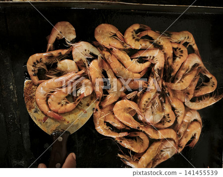 A close-up of cooked, flavorful, and delicious rolled shrimp arranged in various combinations on dark surfaces, showcasing their warm orange-brown hue, textured shells, and natural curves. A close-up of cooked, flavorful, and delicious rolled shrimp arranged in various combinations on dark surfaces, showcasing their warm orange-brown hue, textured shells, and natural curves. 141455539