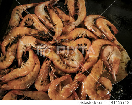 A close-up of cooked, flavorful, and delicious rolled shrimp arranged in various combinations on dark surfaces, showcasing their warm orange-brown hue, textured shells, and natural curves. A close-up of cooked, flavorful, and delicious rolled shrimp arranged in various combinations on dark surfaces, showcasing their warm orange-brown hue, textured shells, and natural curves. 141455540