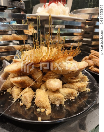 Assorted pastries and traditional Middle Eastern sweets displayed on lavish buffet table in Egyptian hotel, featuring honey drenched treats, nut filled pastes colorful confections under warm lighting Assorted pastries and traditional Middle Eastern sweets displayed on lavish buffet table in Egyptian hotel, featuring honey drenched treats, nut filled pastes colorful confections under warm lighting 141455545