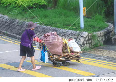 Hong Kong. July 19 2026 Elderly woman pushing heavy cart Hong Kong. July 19 2026 Elderly woman pushing heavy cart 141457326