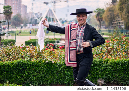 Portrait of a smiling, cheerful young man dressed as a Chilean huaso, celebrating and posing to dance cueca, a traditional Chilean dance. Chilean traditions, celebration, and culture. Portrait of a smiling, cheerful young man dressed as a Chilean huaso, celebrating and posing to dance cueca, a traditional Chilean dance. Chilean traditions, celebration, and culture. 141458106