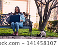 A beautiful Latina executive working remotely from home, in her backyard, with her laptop, next to her cat, touching it, joy, affection. Teleworking, marketing. 141458107