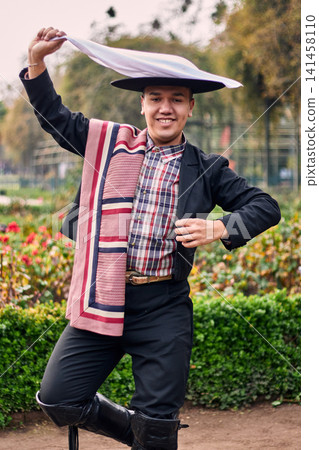 Portrait of a smiling, cheerful young man dressed as a Chilean huaso, celebrating and posing to dance cueca, a traditional Chilean dance. Chilean traditions, celebration, and culture. Portrait of a smiling, cheerful young man dressed as a Chilean huaso, celebrating and posing to dance cueca, a traditional Chilean dance. Chilean traditions, celebration, and culture. 141458110