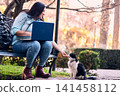 A beautiful Latina executive working remotely from home, in her backyard, with her laptop, next to her cat, touching it, joy, affection. Teleworking, marketing. 141458112