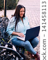 A beautiful Latina executive working remotely from home, in her backyard, with her laptop, next to her cat, touching it, joy, affection. Teleworking, marketing. 141458113