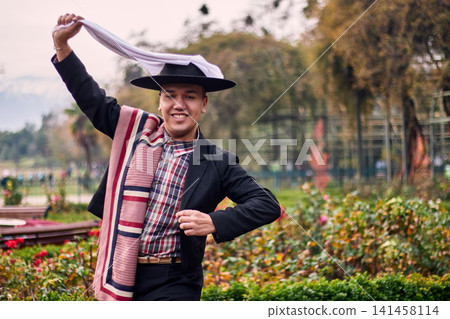 Portrait of a smiling, cheerful young man dressed as a Chilean huaso, celebrating and posing to dance cueca, a traditional Chilean dance. Chilean traditions, celebration, and culture. Portrait of a smiling, cheerful young man dressed as a Chilean huaso, celebrating and posing to dance cueca, a traditional Chilean dance. Chilean traditions, celebration, and culture. 141458114