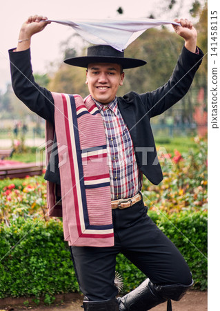 Portrait of a smiling, cheerful young man dressed as a Chilean huaso, celebrating and posing to dance cueca, a traditional Chilean dance. Chilean traditions, celebration, and culture. Portrait of a smiling, cheerful young man dressed as a Chilean huaso, celebrating and posing to dance cueca, a traditional Chilean dance. Chilean traditions, celebration, and culture. 141458115