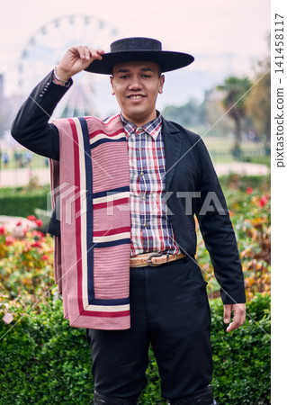 Portrait of a smiling, cheerful young man dressed as a Chilean huaso, celebrating and posing to dance cueca, a traditional Chilean dance. Chilean traditions, celebration, and culture. Portrait of a smiling, cheerful young man dressed as a Chilean huaso, celebrating and posing to dance cueca, a traditional Chilean dance. Chilean traditions, celebration, and culture. 141458117
