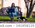 A beautiful Latina executive working remotely from home, in her backyard, with her laptop, next to her cat, touching it, joy, affection. Teleworking, marketing. 141458119