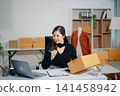 Asian online seller managing e-commerce business from home with laptop and shipping boxes. Live selling, social media marketing, order fulfillment and small business concept. 141458942