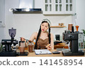 Young Asian female barista preparing fresh roasted coffee beans in a modern cafe kitchen with professional espresso equipment. 141458954