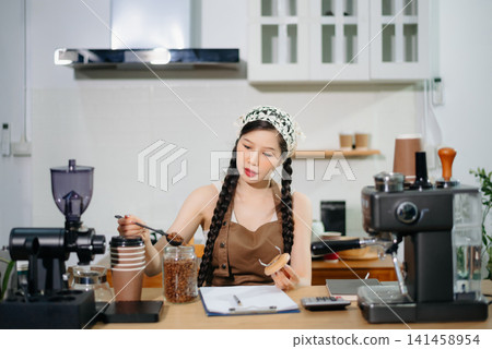 Young Asian female barista preparing fresh roasted coffee beans in a modern cafe kitchen with professional espresso equipment. Young Asian female barista preparing fresh roasted coffee beans in a modern cafe kitchen with professional espresso equipment. 141458954