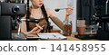 Young Asian female barista preparing fresh roasted coffee beans in a modern cafe kitchen with professional espresso equipment. 141458955