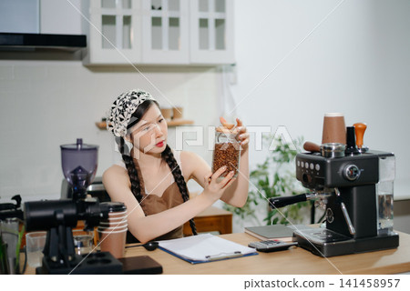 Young Asian female barista preparing fresh roasted coffee beans in a modern cafe kitchen with professional espresso equipment. Young Asian female barista preparing fresh roasted coffee beans in a modern cafe kitchen with professional espresso equipment. 141458957
