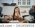 Young Asian female barista preparing fresh roasted coffee beans in a modern cafe kitchen with professional espresso equipment. 141458958