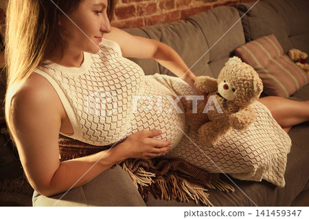 Pregnant woman resting with teddy bear and hand on belly 141459347