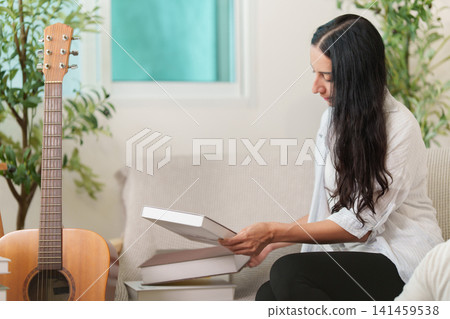 Indian woman reading book on sofa at home with guitar Indian woman reading book on sofa at home with guitar 141459538