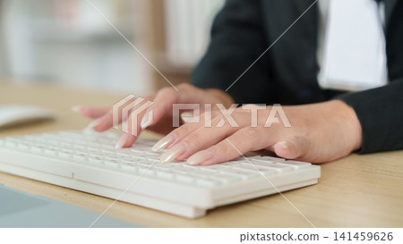 Cropped hands with manicured nails typing on white keyboard at wooden desk Cropped hands with manicured nails typing on white keyboard at wooden desk 141459626